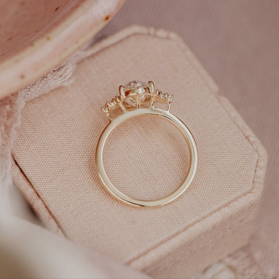 Top-down view focused on the yellow gold band of a diamond engagement ring set on a pink ring box