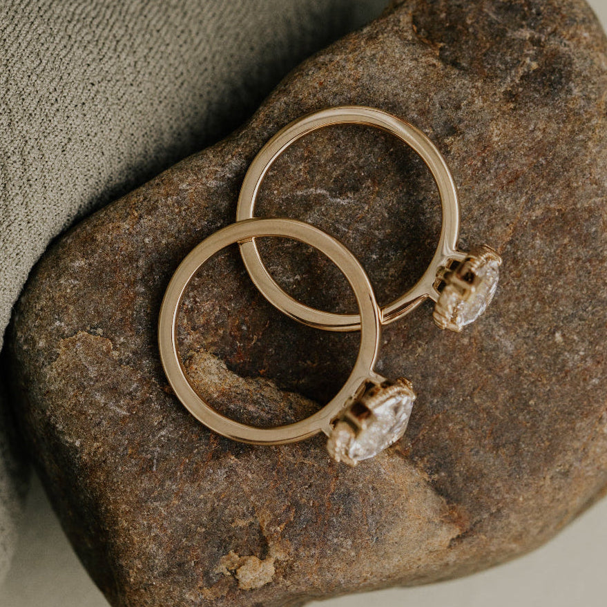 Two gold engagement rings with diamonds on a textured stone surface