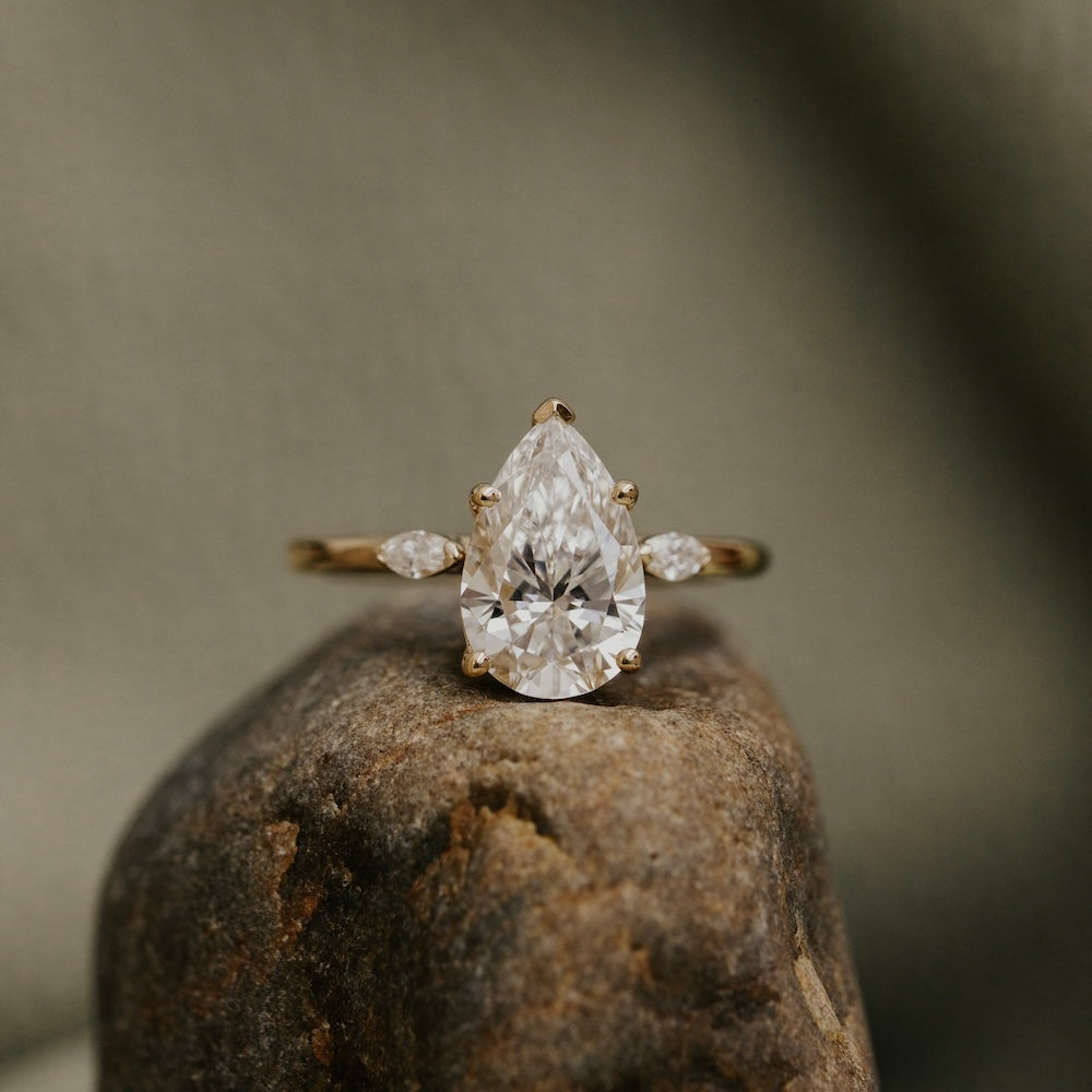 Diamond ring with a pear-shaped center stone on a textured surface