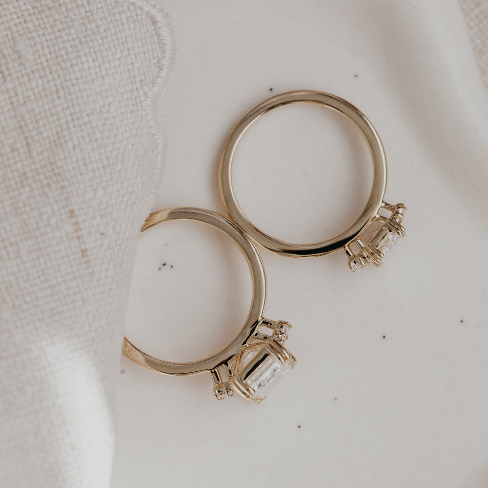 Top-down view of two yellow gold engagement rings on a white surface