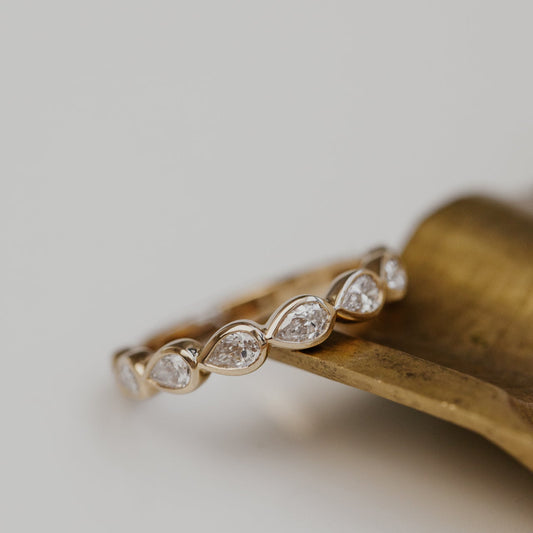 Gold wedding band with pear diamond stones on a wooden surface