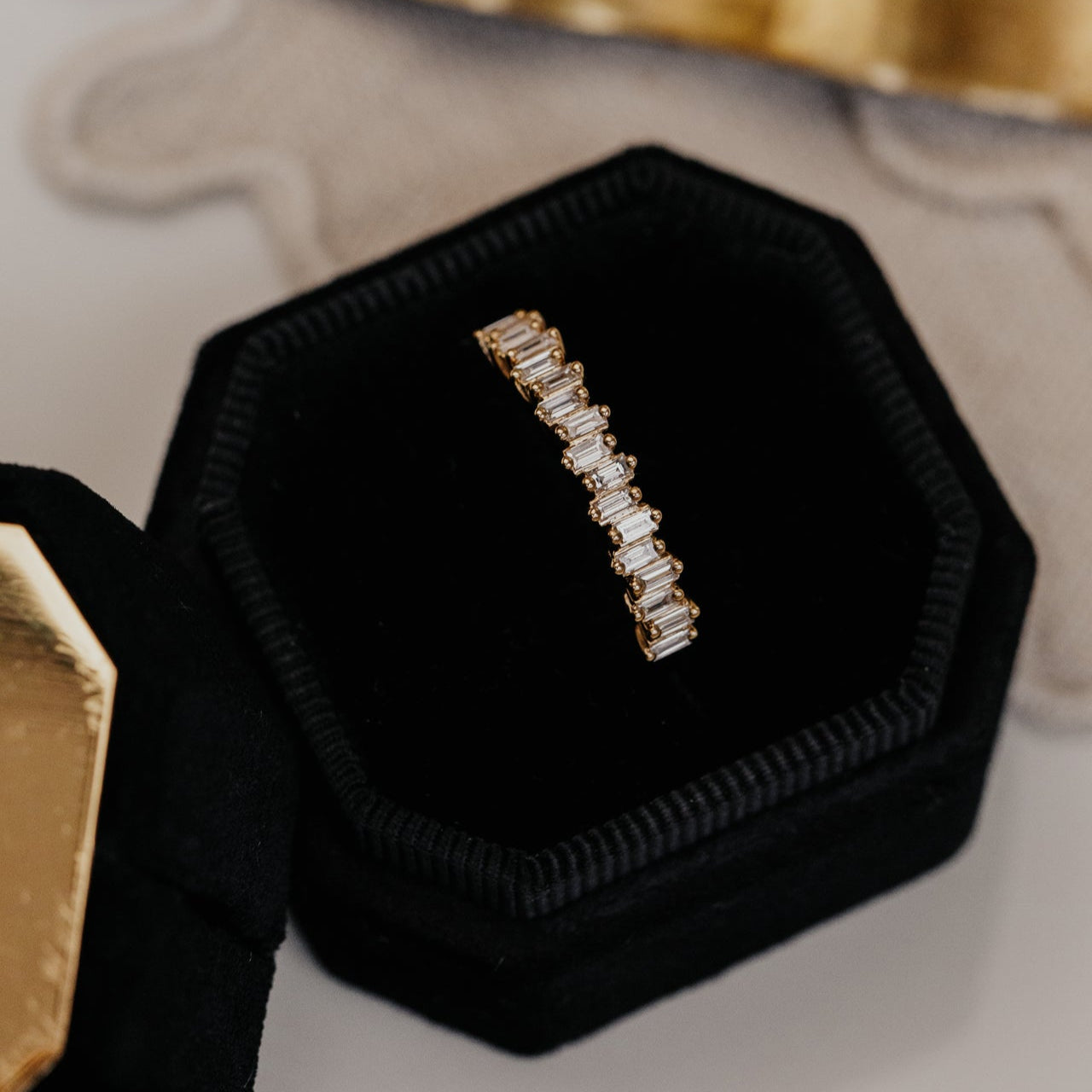Diamond wedding band in a black hexagonal jewelry box on a neutral background