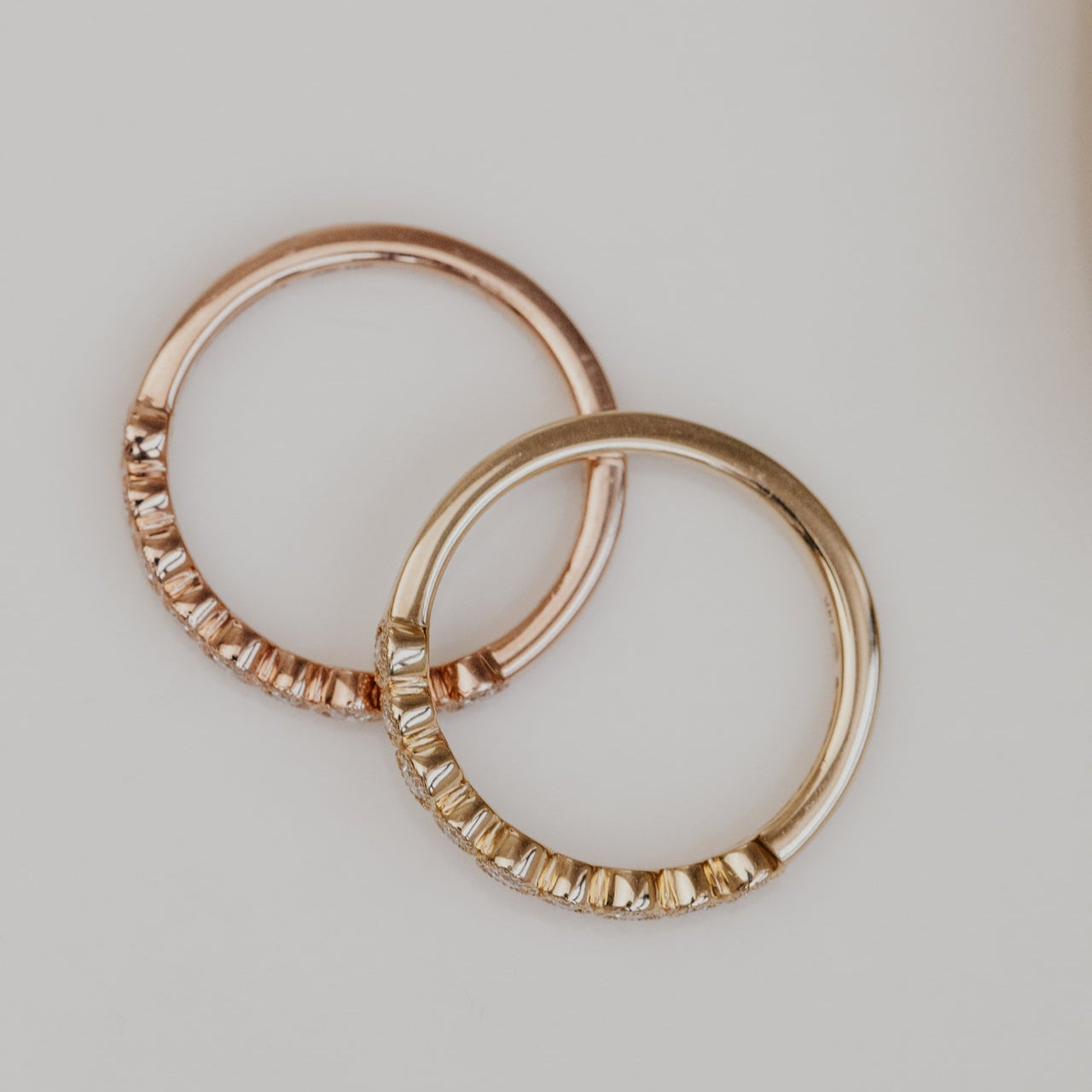 Two gold wedding bands with embedded stones on a light background
