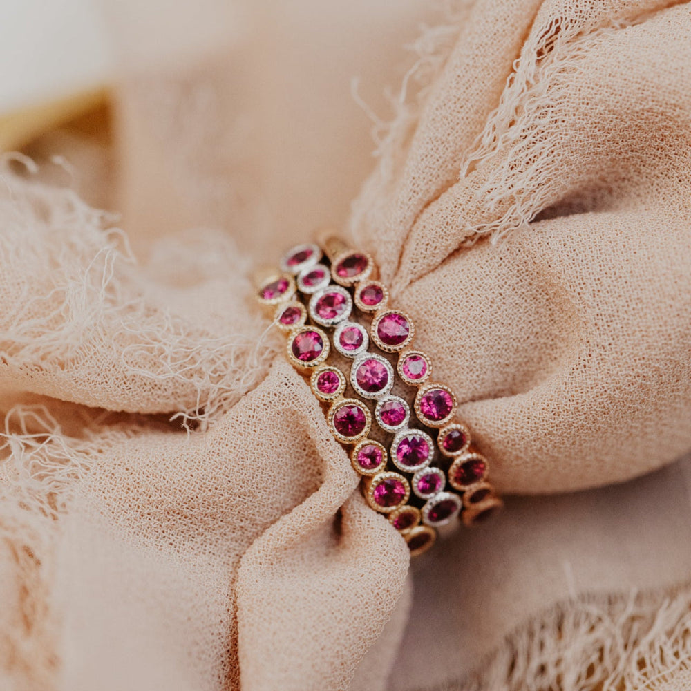 Ruby red gemstone band in 14k white, yellow, and rose gold on a beige fabric background