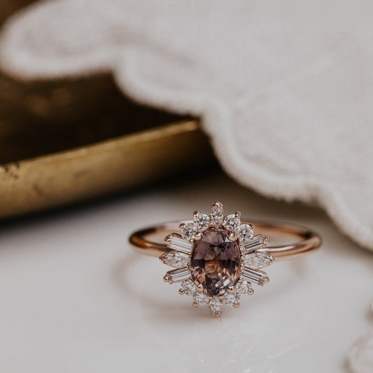 Rose gold ring with a purple sapphire gemstone and diamond halo on a soft fabric background