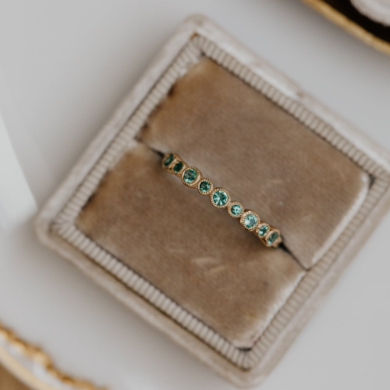 Gold wedding band with green emerald gemstones in a jewelry box