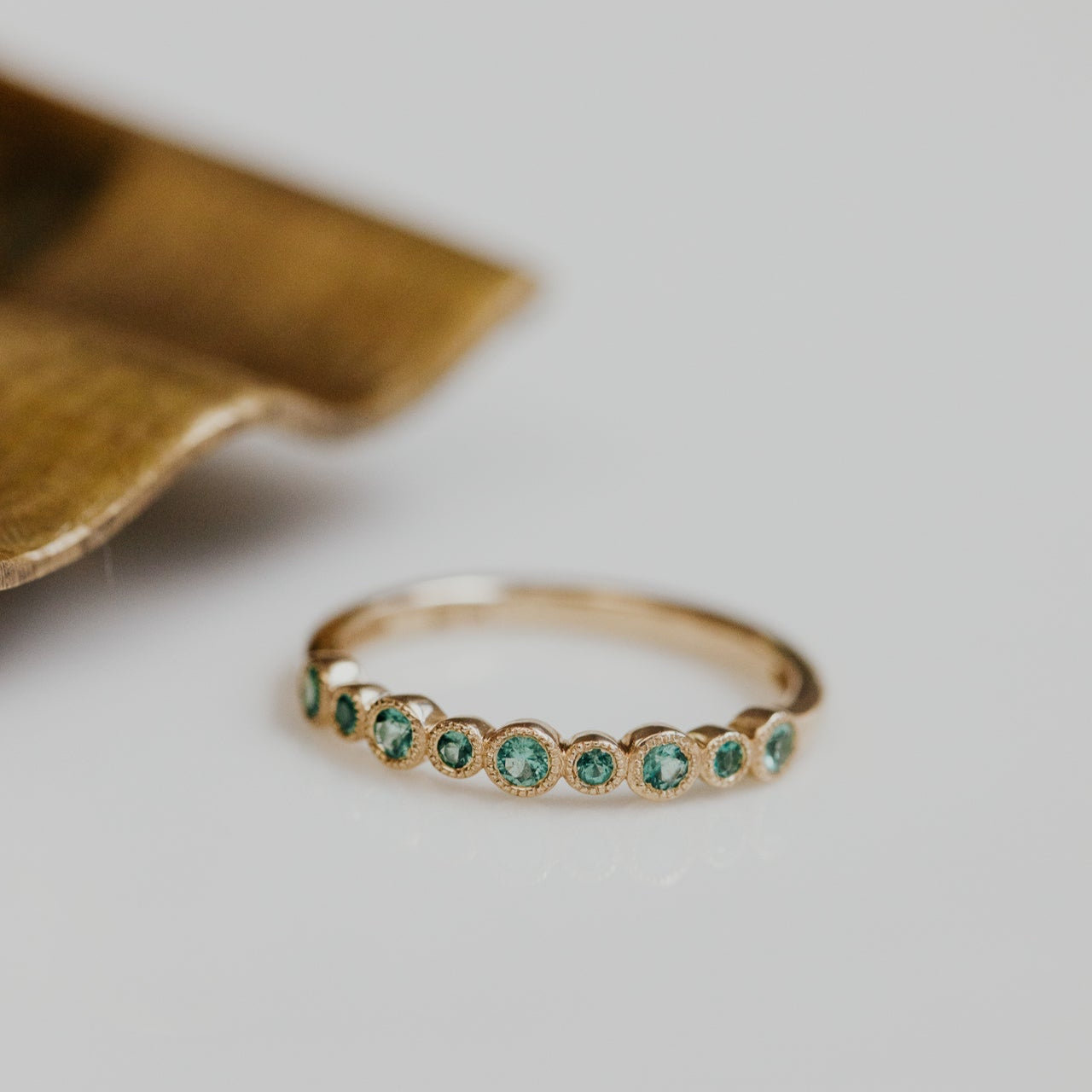 Gold ring with green  emerald gemstones on a light background