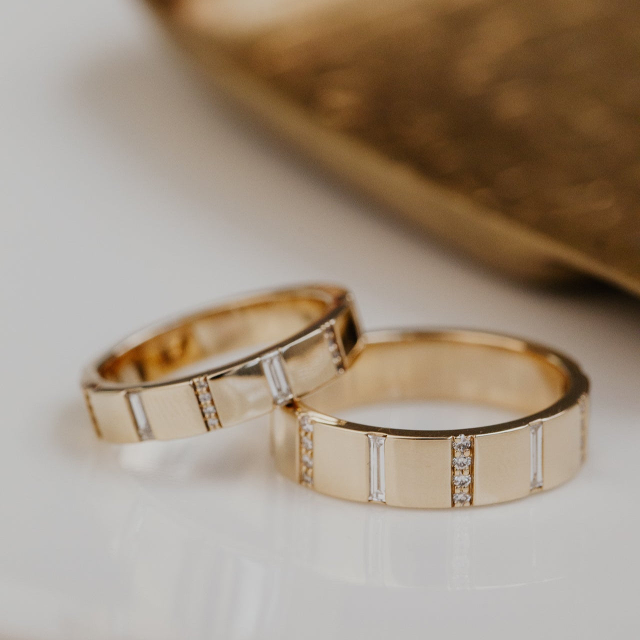 Two gold wedding bands with diamond accents on a light background