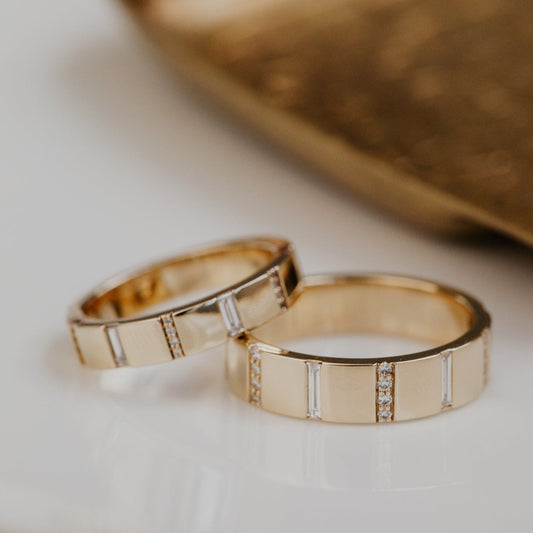 Two gold wedding bands with diamond accents on a light background