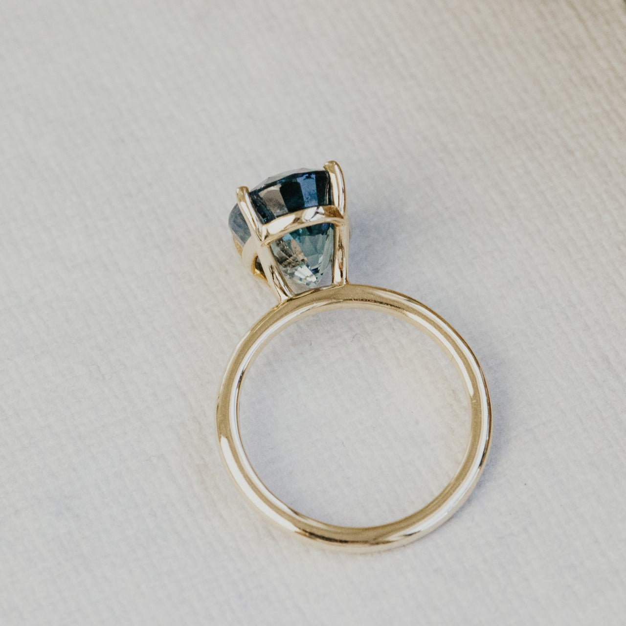 Gold ring with a blue sapphire gemstone on a textured beige surface