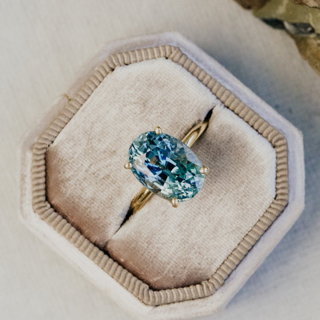 Gold ring with a large blue sapphire gemstone in a hexagonal jewelry box.