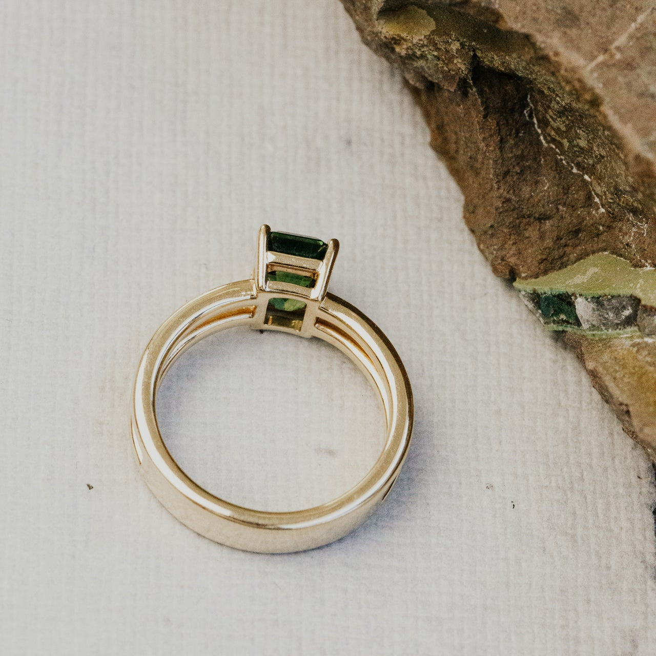 Gold ring with green sapphire gemstone on a textured surface