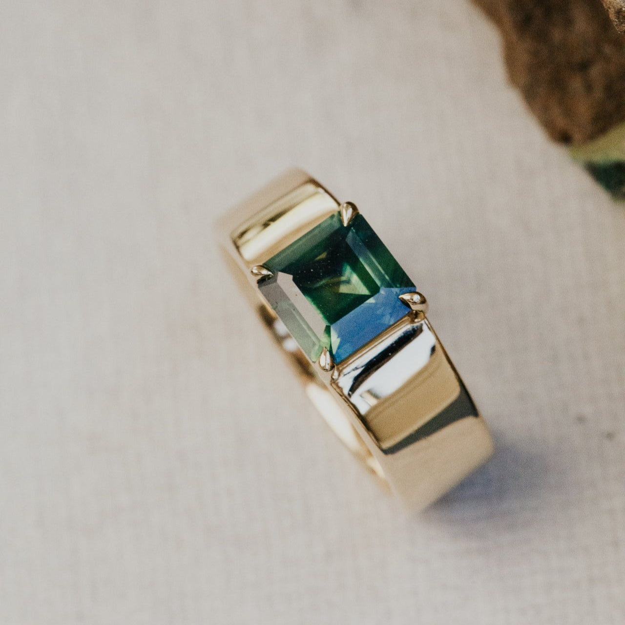 Gold ring with a green sapphire gemstone on a neutral background