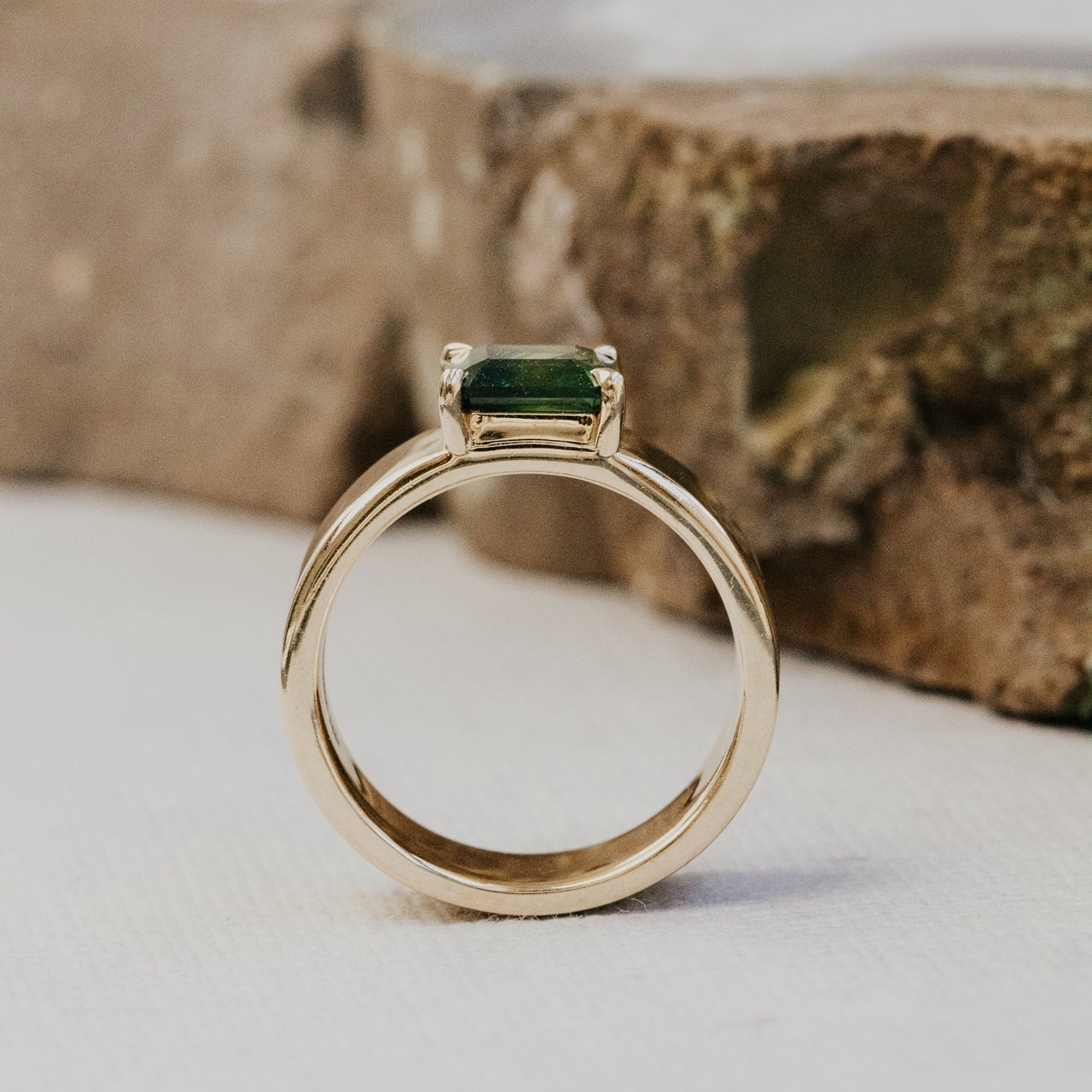 Gold ring with a green sapphire gemstone on a neutral background