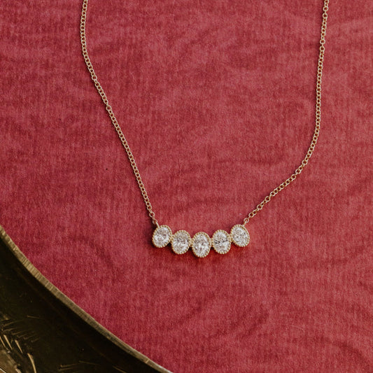 Gold necklace with four oval diamonds on a red textured surface