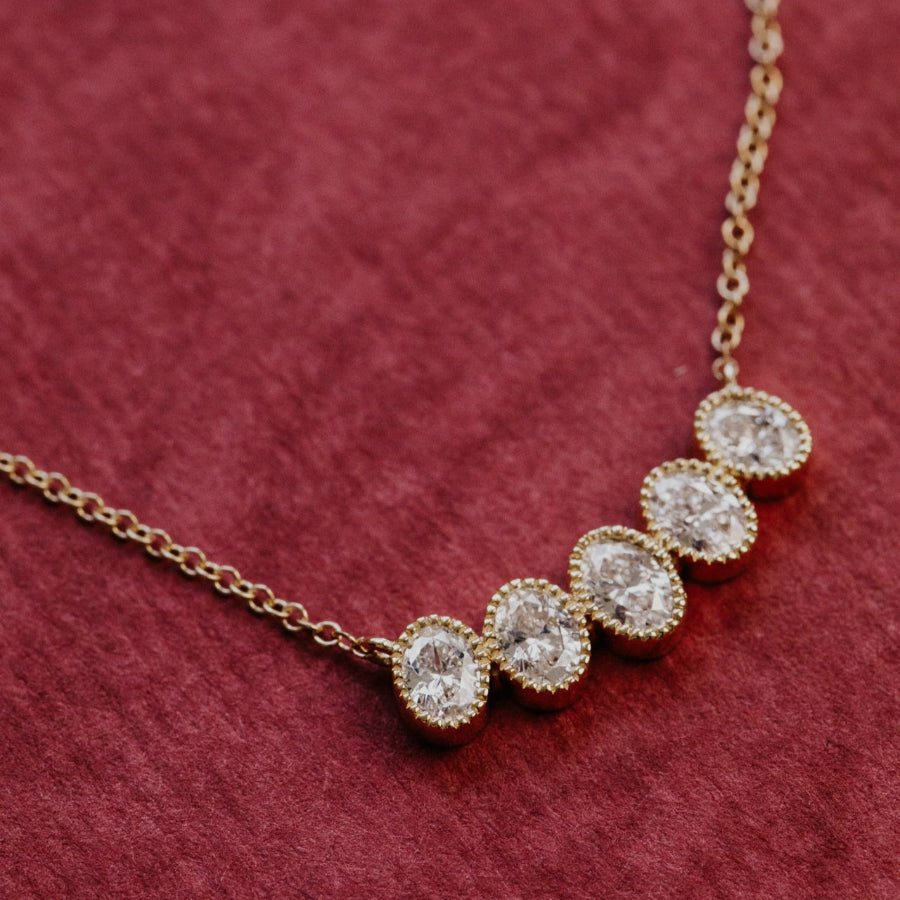 Gold necklace with oval diamonds on a red textured background