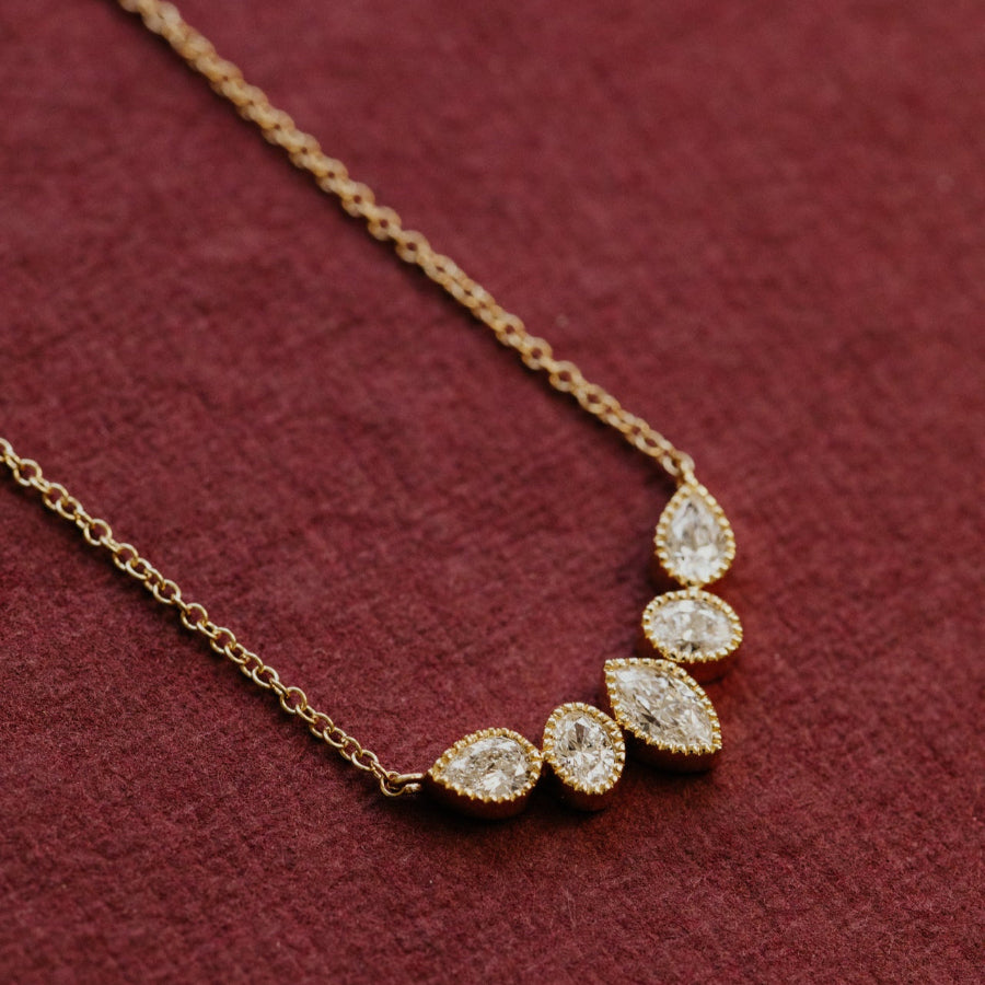 Gold necklace with teardrop-shaped diamond pendants on a red background