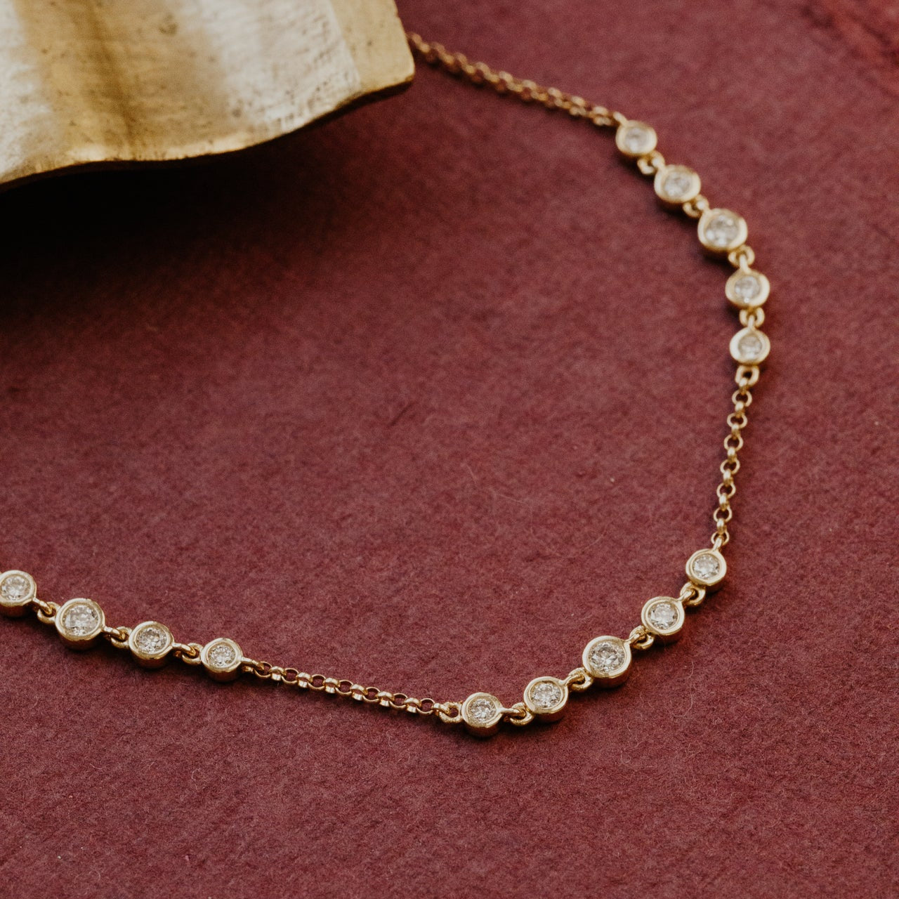 Gold diamond bracelet with small diamonds on a maroon surface