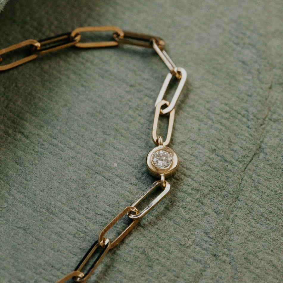 Gold chain bracelet with a diamond on a textured green surface