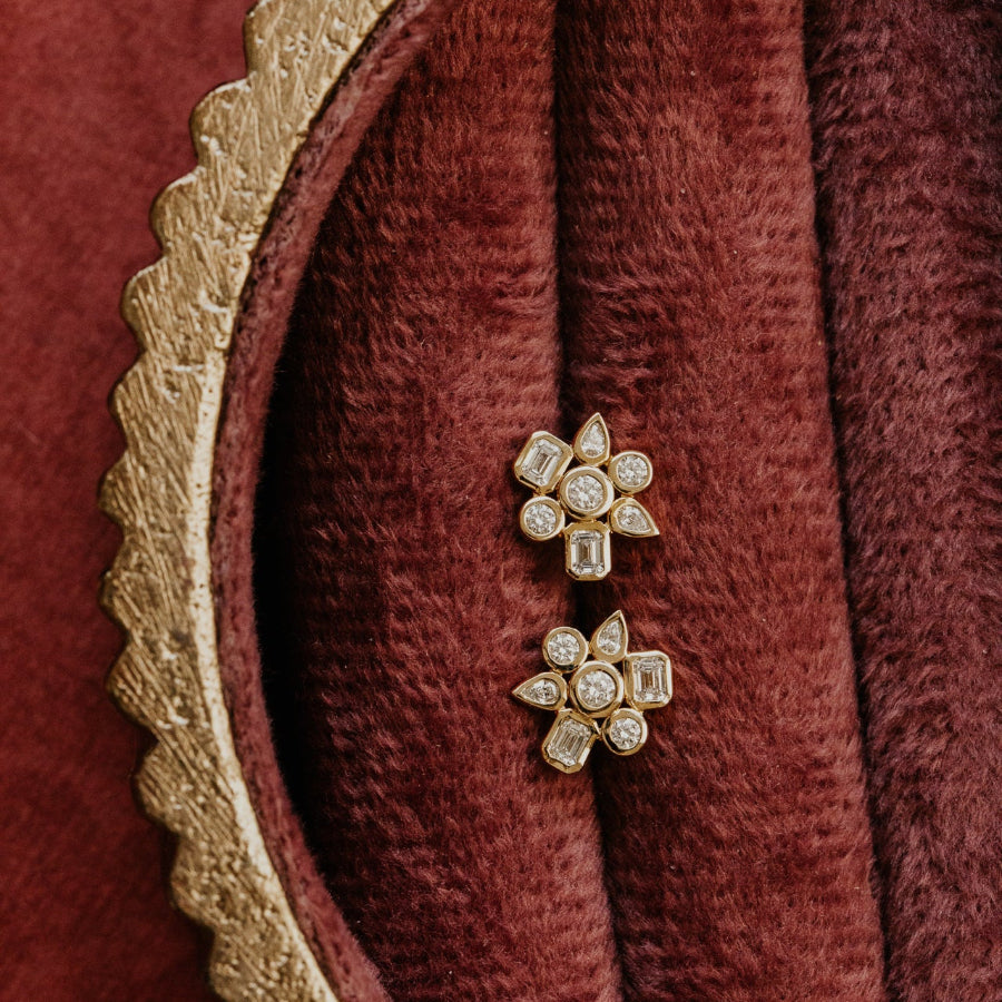 Gold earrings with diamonds on a maroon fabric background