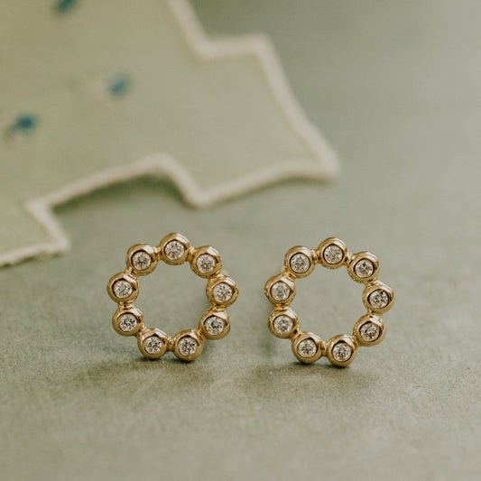 Gold round stud earrings with small diamonds on a textured surface