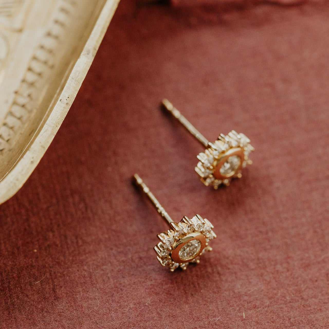 Pair of gold earrings with diamond stones on a textured red surface.
