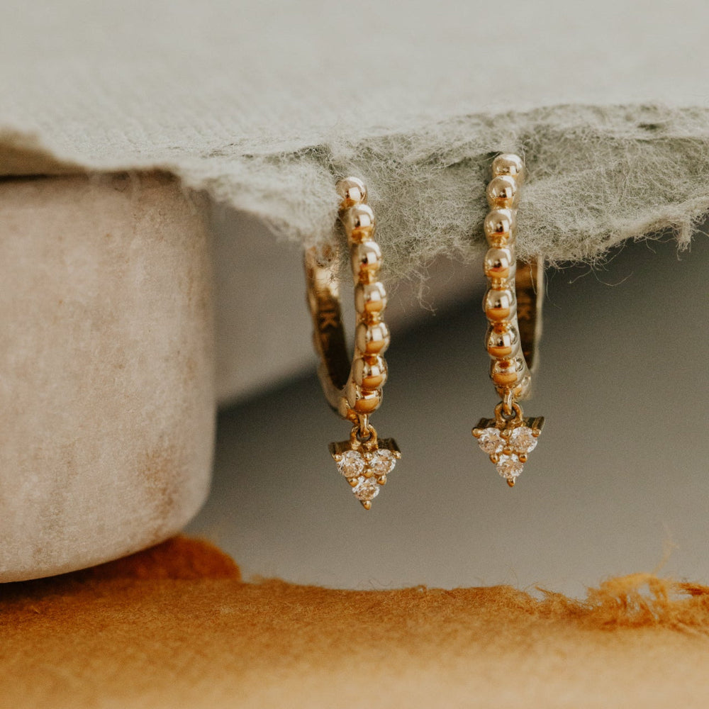 Gold hoop diamond clusters earrings on a textured surface with a neutral background