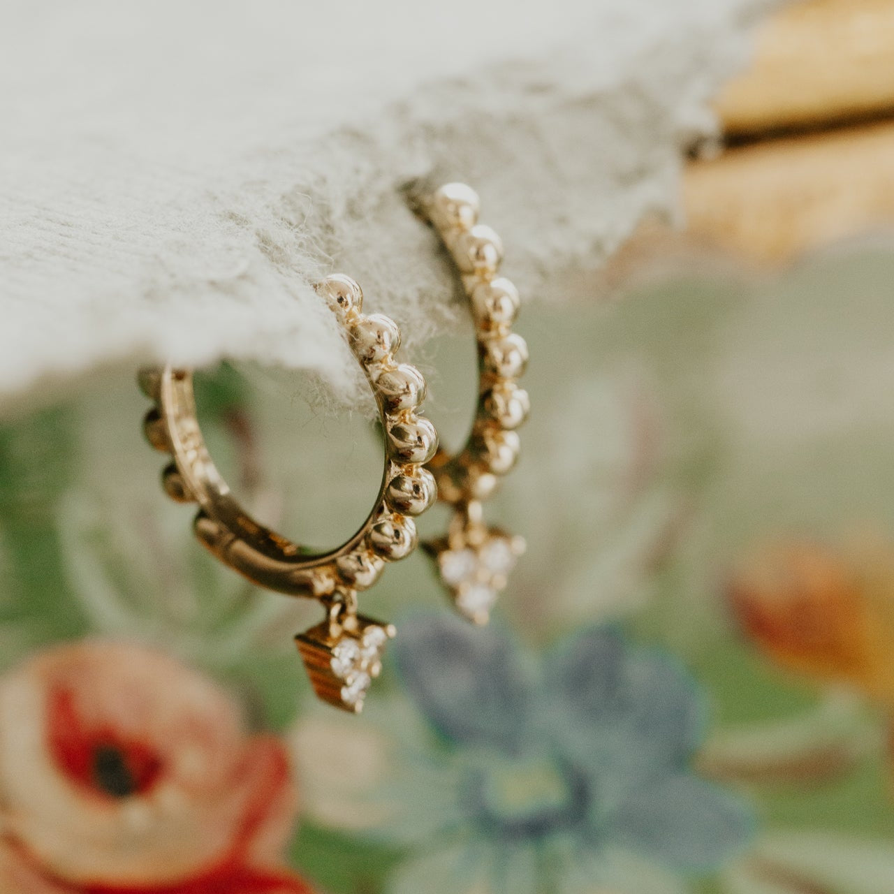 Gold hoop earrings with diamond cluster accents on a floral background