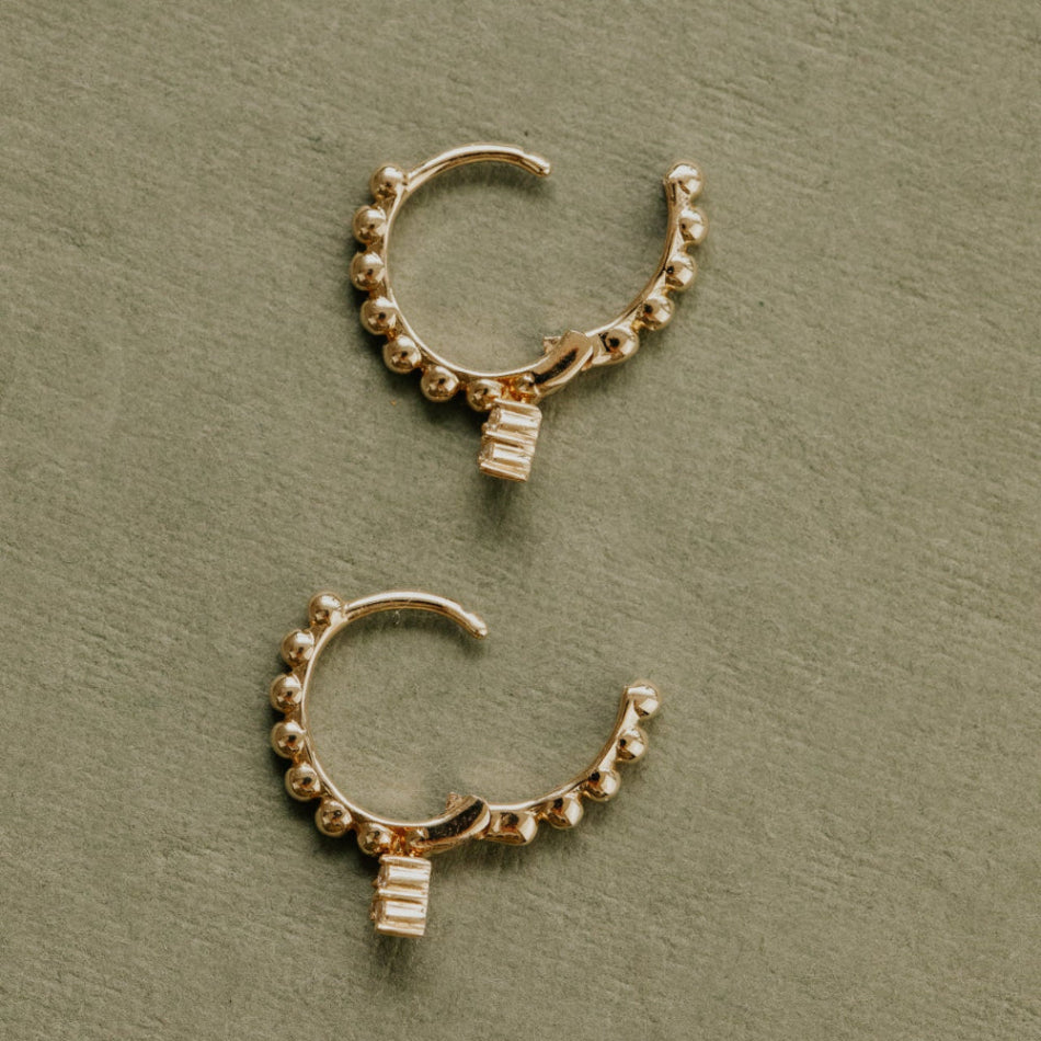 Pair of gold hoop earrings with small stones on a green background