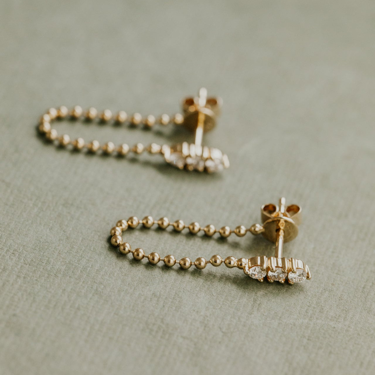 Gold earrings with beaded design on a textured surface