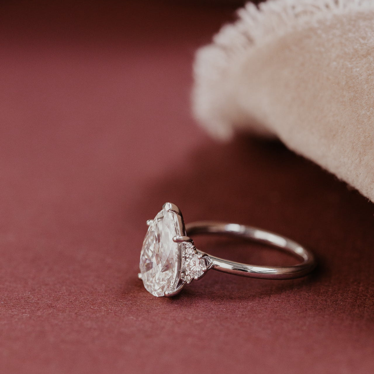 Pear shaped diamond ring on a textured red surface with a beige fabric background