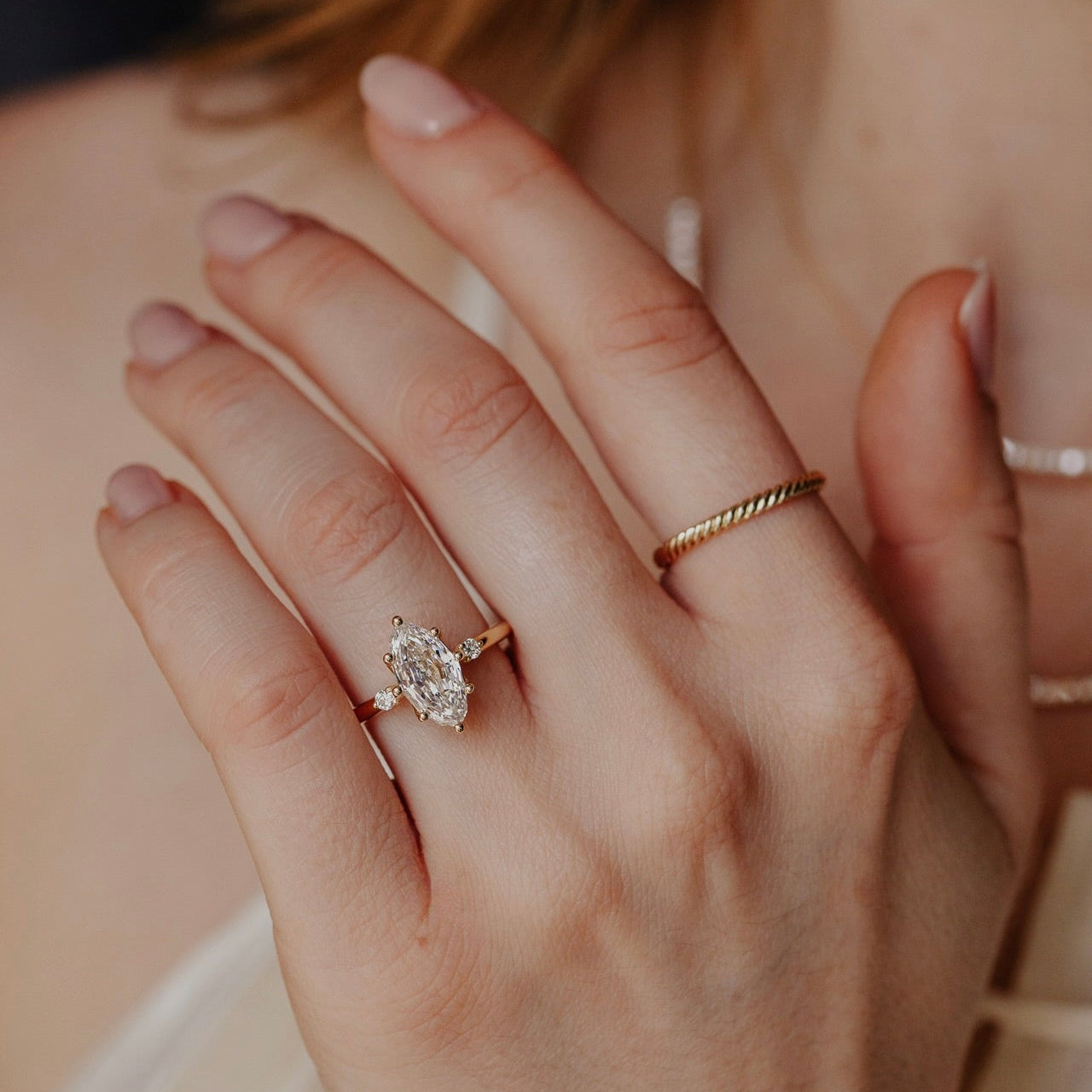 Close-up of a hand wearing a marquise diamond ring with a blurred background