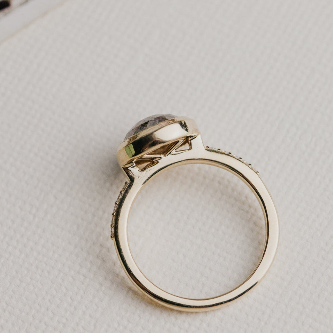 14k gold ring featuring a round grey rustic diamond set in a milgrain bezel with a .09 cttw pave diamond band.