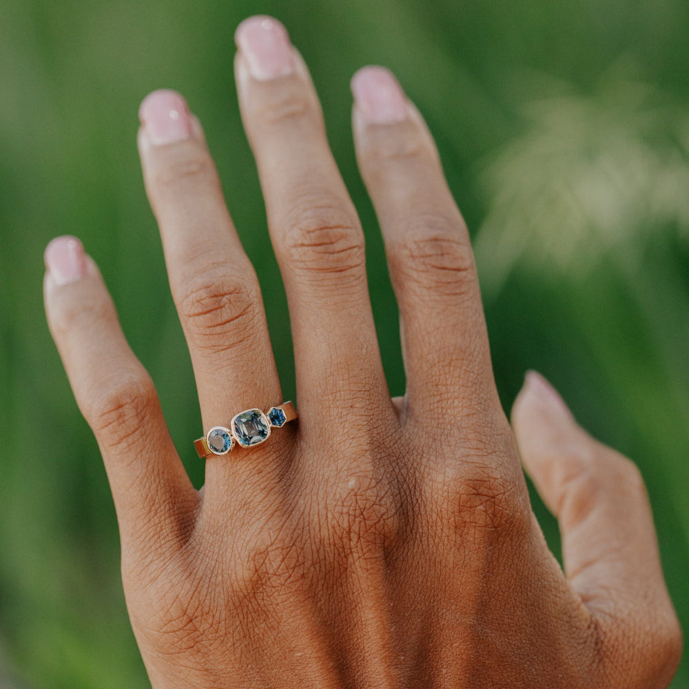 Hand wearing a ring with blue gemstones against a blurred green background
