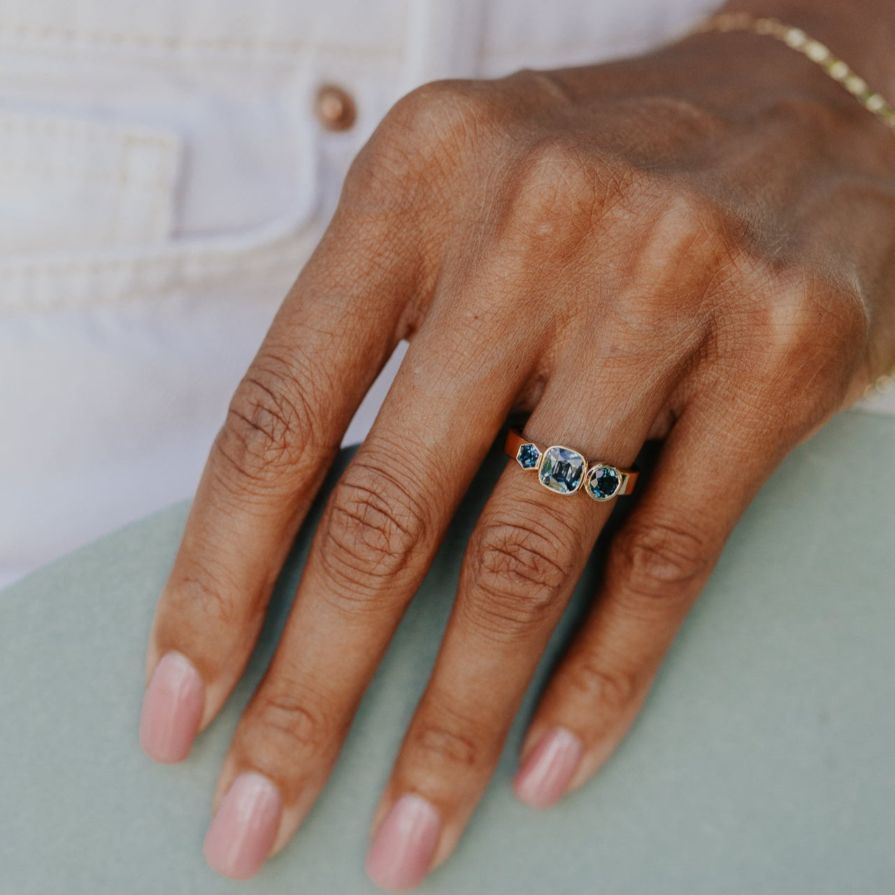 Hand wearing a ring with a cushion blue Australian sapphire gemstones on a light background