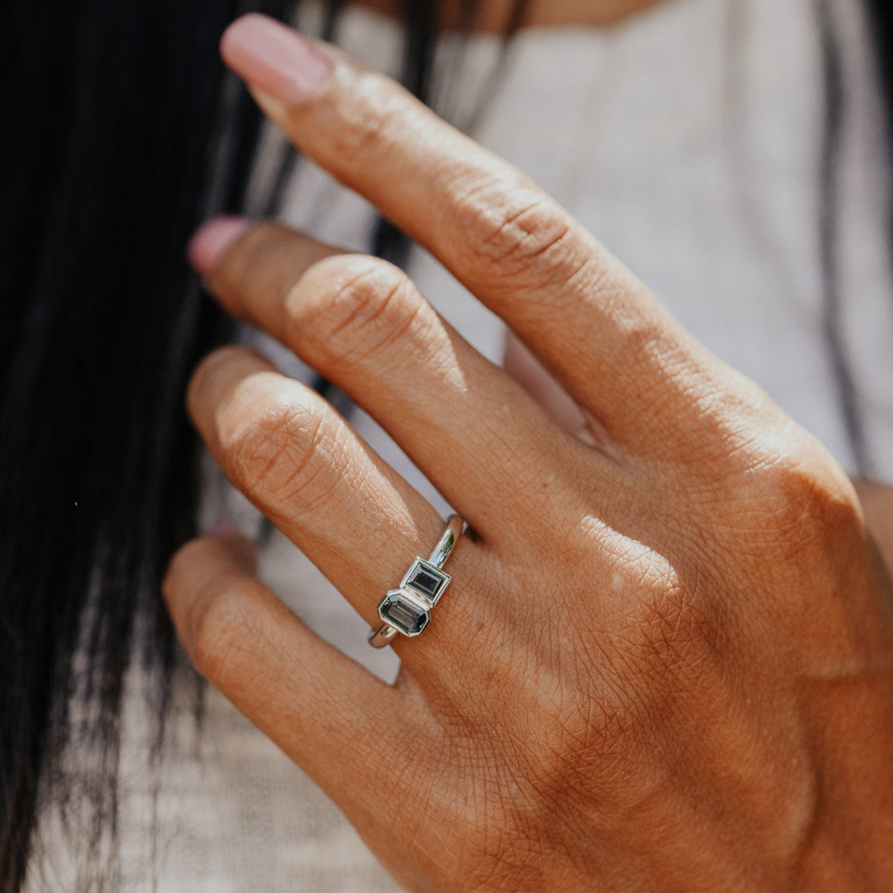 Close-up of a hand wearing a white gold ring with a blue and green sapphires.