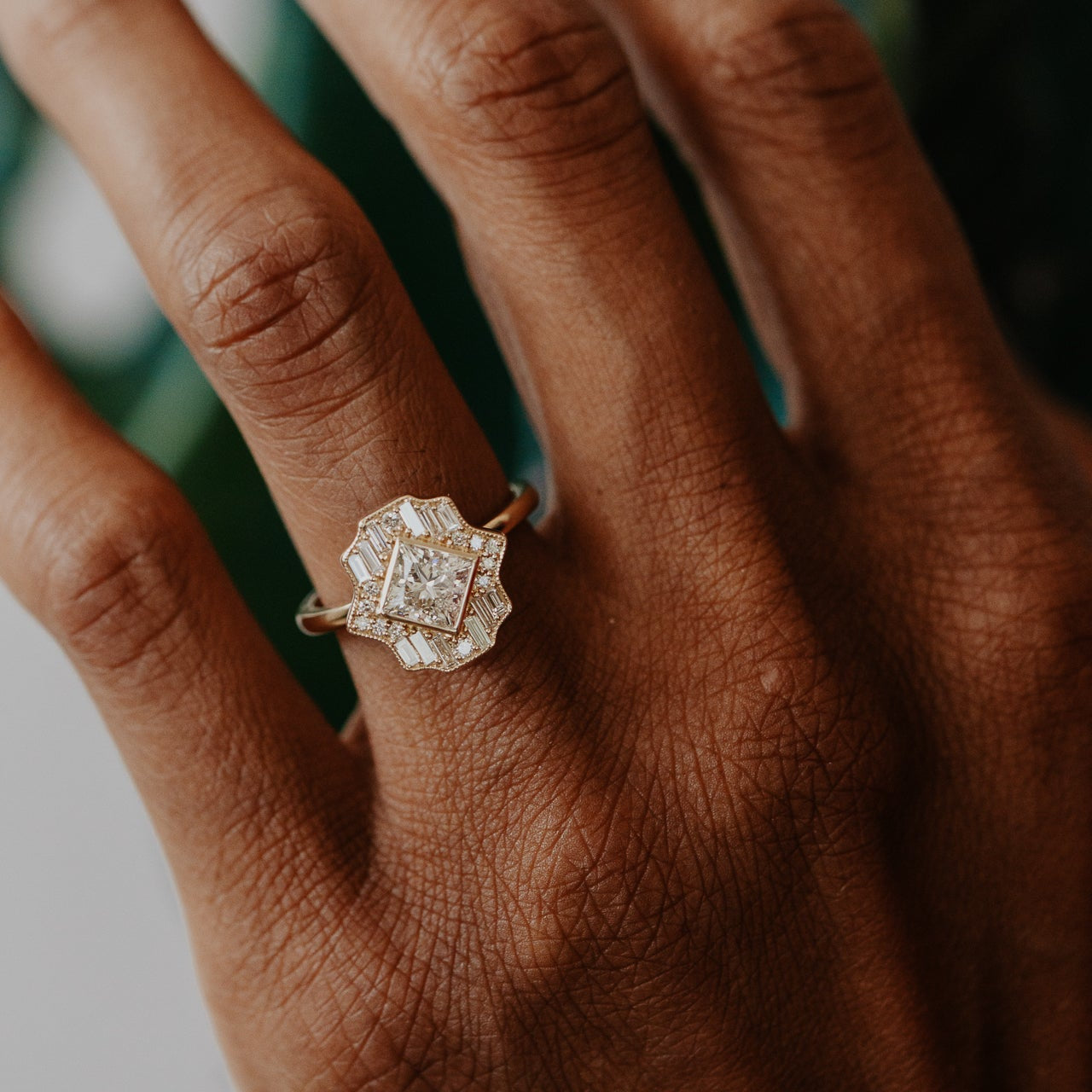 Close-up of a hand wearing a diamond halo ring with a blurred background