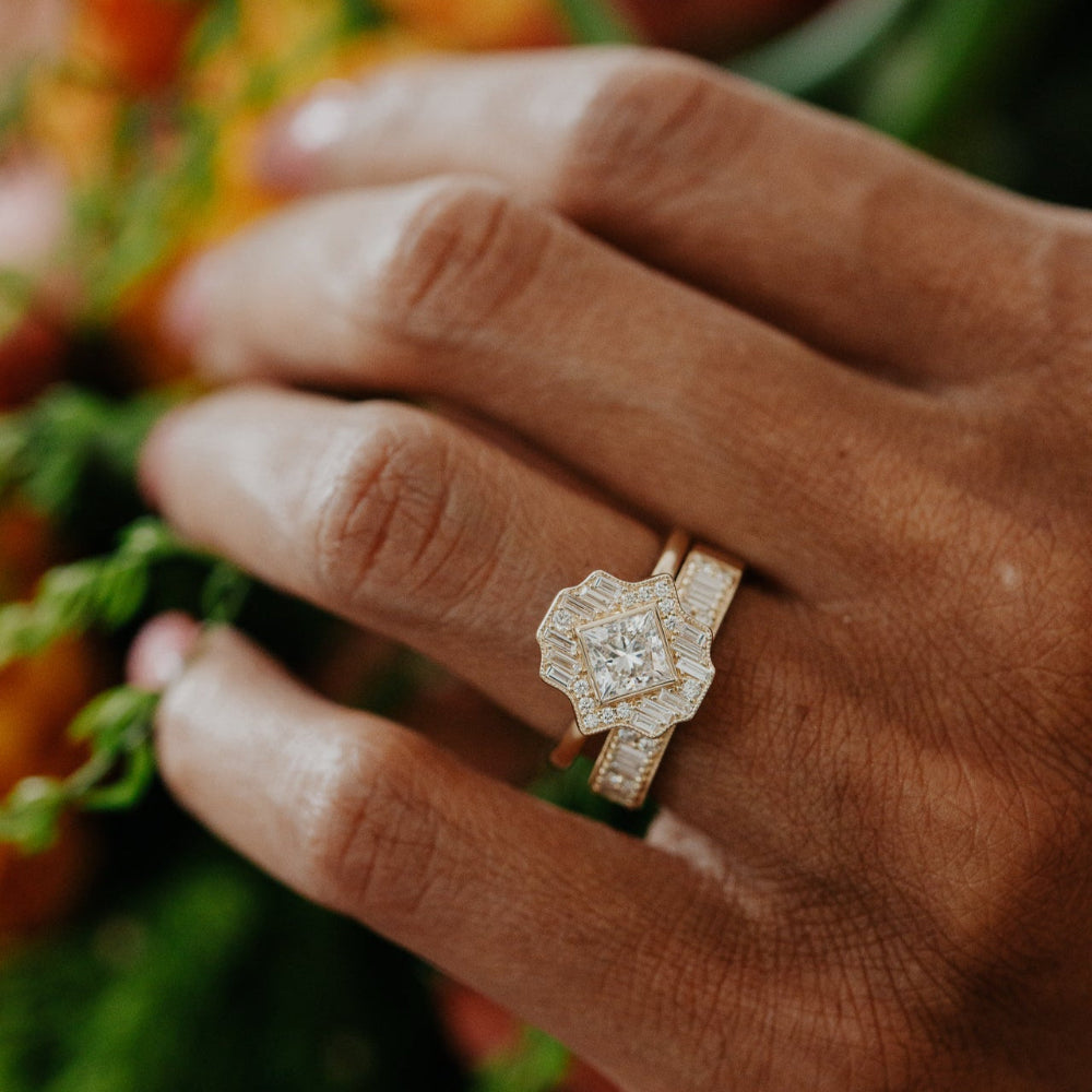 Hand wearing a gold ring with a diamond, halo surrounded by a green backgound