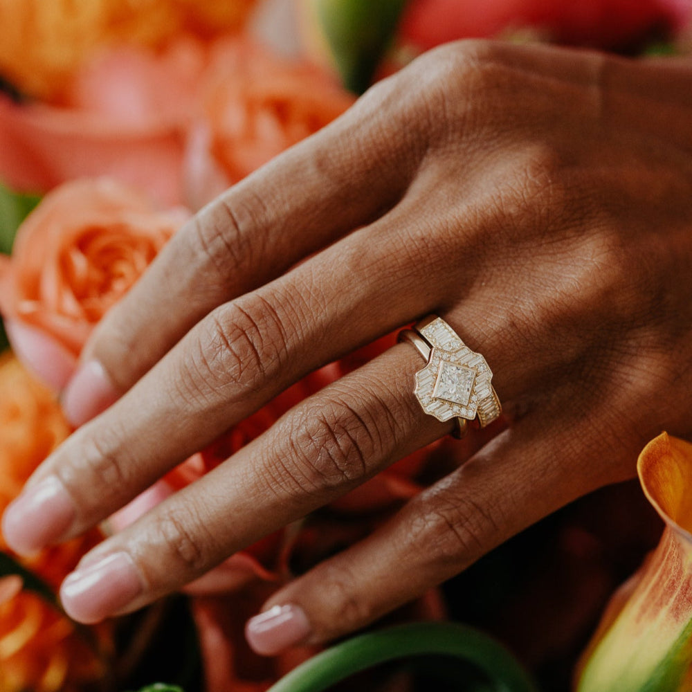 Hand wearing a diamond ring and band on a background of orange flowers
