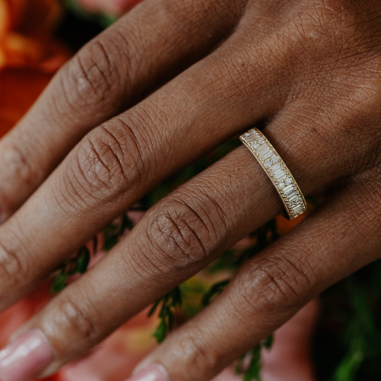 Close-up of a hand wearing a gold diamond band with a blurred floral background