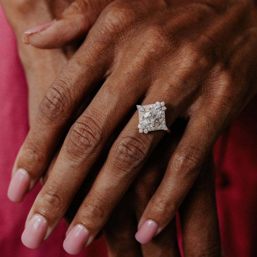 Close-up of a hand wearing a marquise diamond ring against a red background