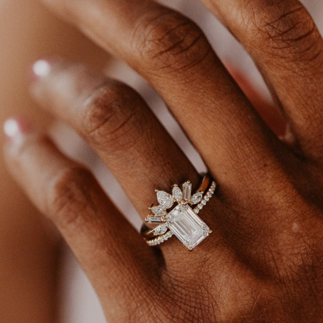 14k gold wedding band featuring pear, marquise, and baguette diamonds set in prongs in a starburst design paired with a emerald cut diamond solitaire ring