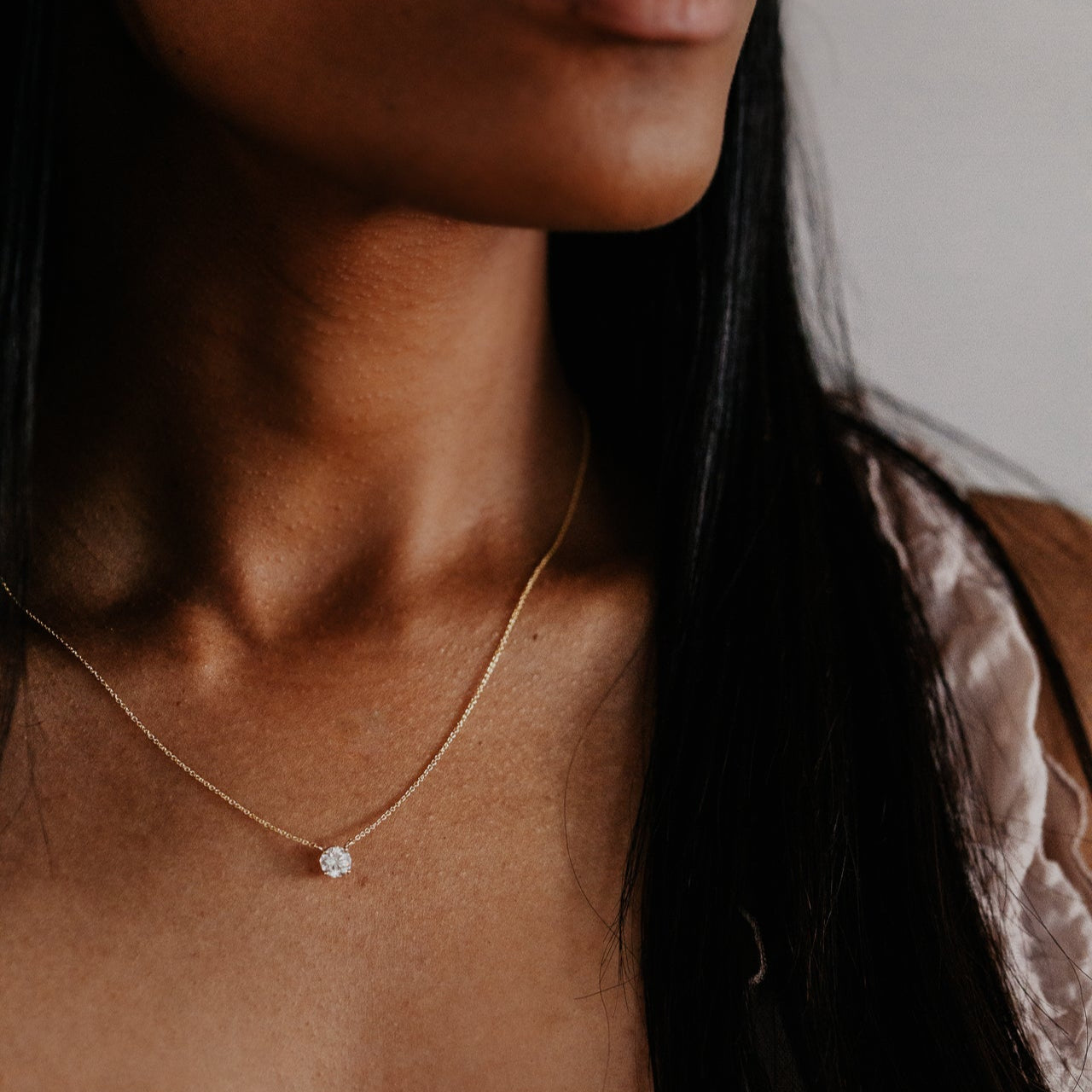 Close-up of a person wearing a delicate gold necklace with a diamond pendant.