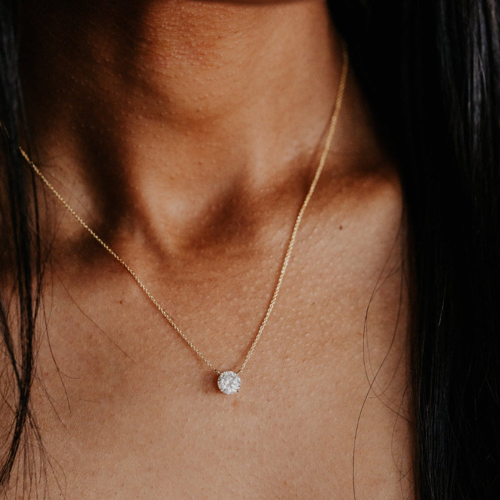 Close-up of a gold necklace with a diamond pendant on a person's neck.