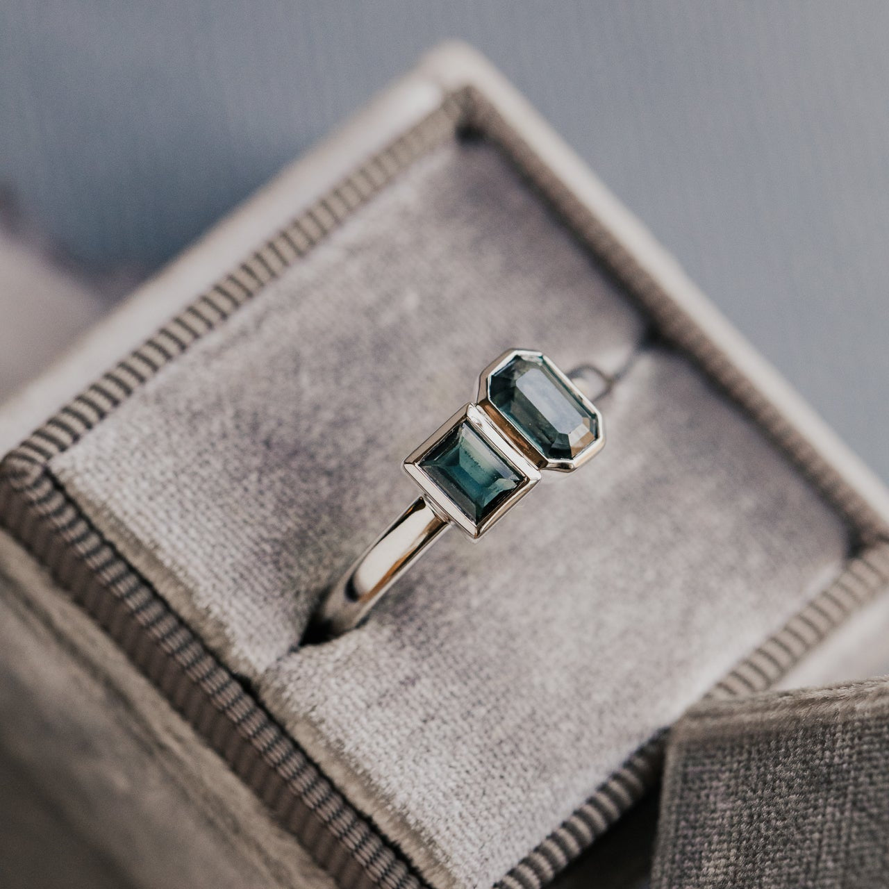 White gold ring with green and blue sapphires in a jewelry box