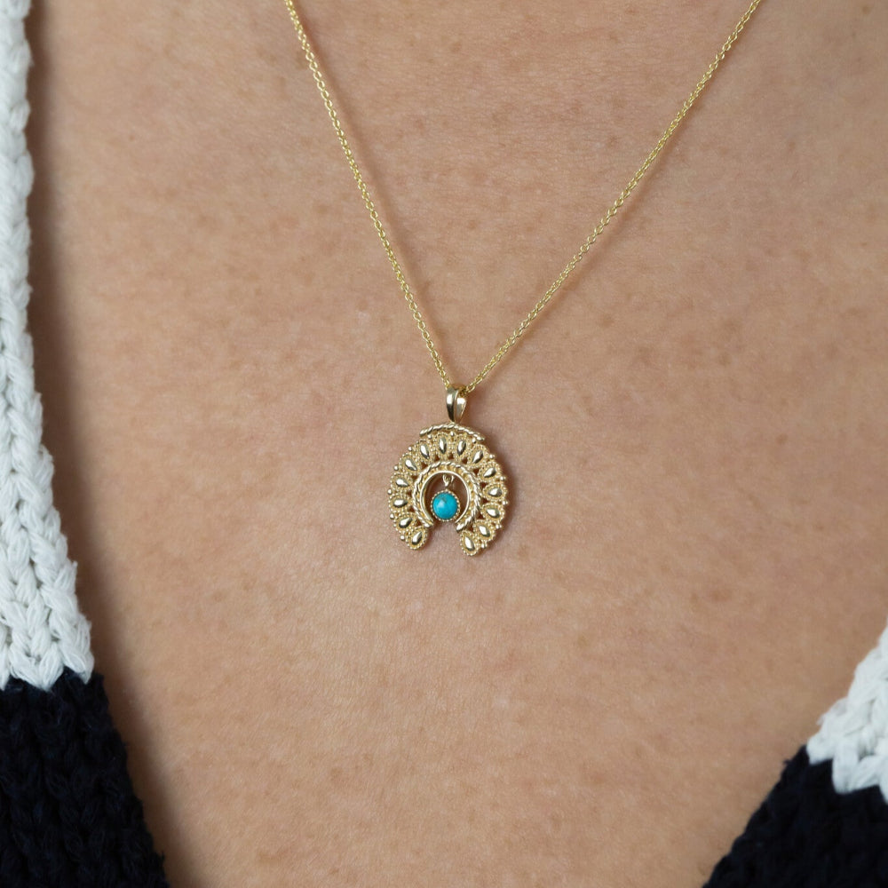 Gold necklace with a turquoise pendant on a person wearing a black and white top.