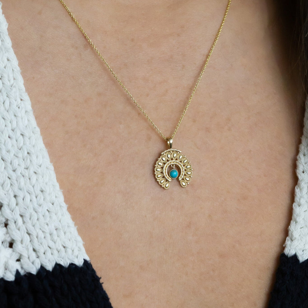 Gold necklace with a blue gemstone pendant on a person wearing a black and white top.