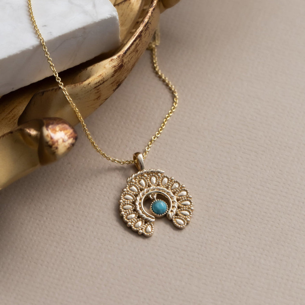 Gold necklace with a turquoise pendant on a beige surface