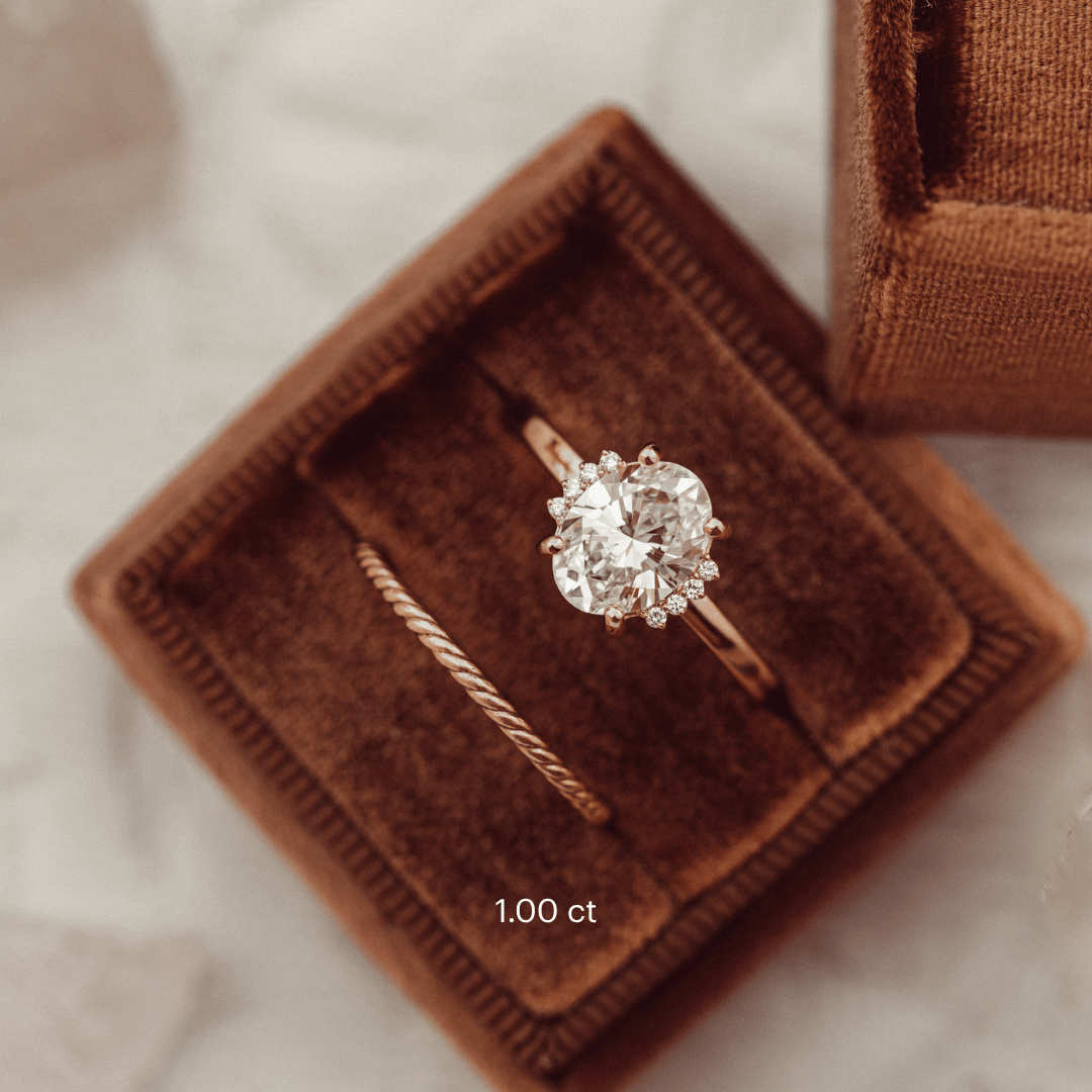 The Claire Oval Ring in 14k rose gold featuring a lab grown diamond oval center stone with starburst-set accent diamonds, displayed in a brown velvet ring box alongside a twisted stacking band.