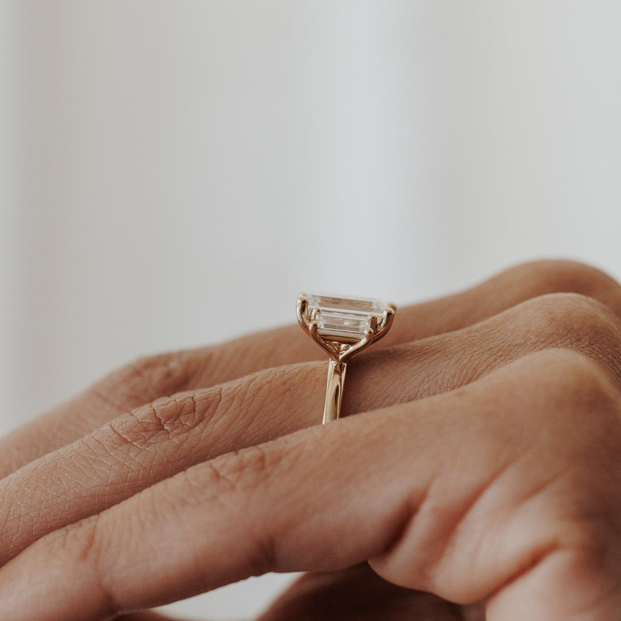 The Hannah Emerald Cut Ring in 14k yellow gold worn on the ring finger, shown from a side profile angle against a white background.